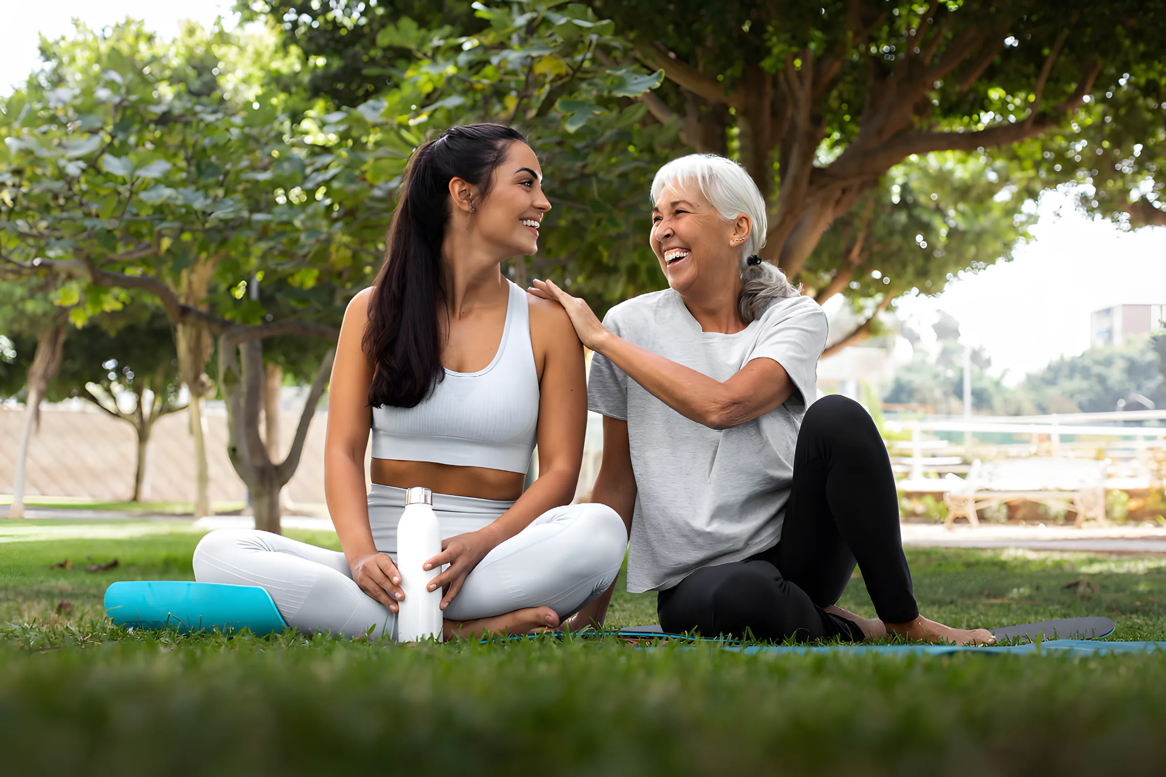 Duas mulheres, uma jovem e uma idosa, sorrindo sentadas na grama depois de um exercício ao ar livre